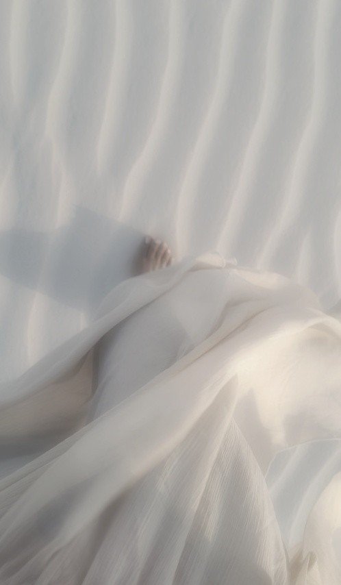 A hand emerging from white fabric draped over sand dunes